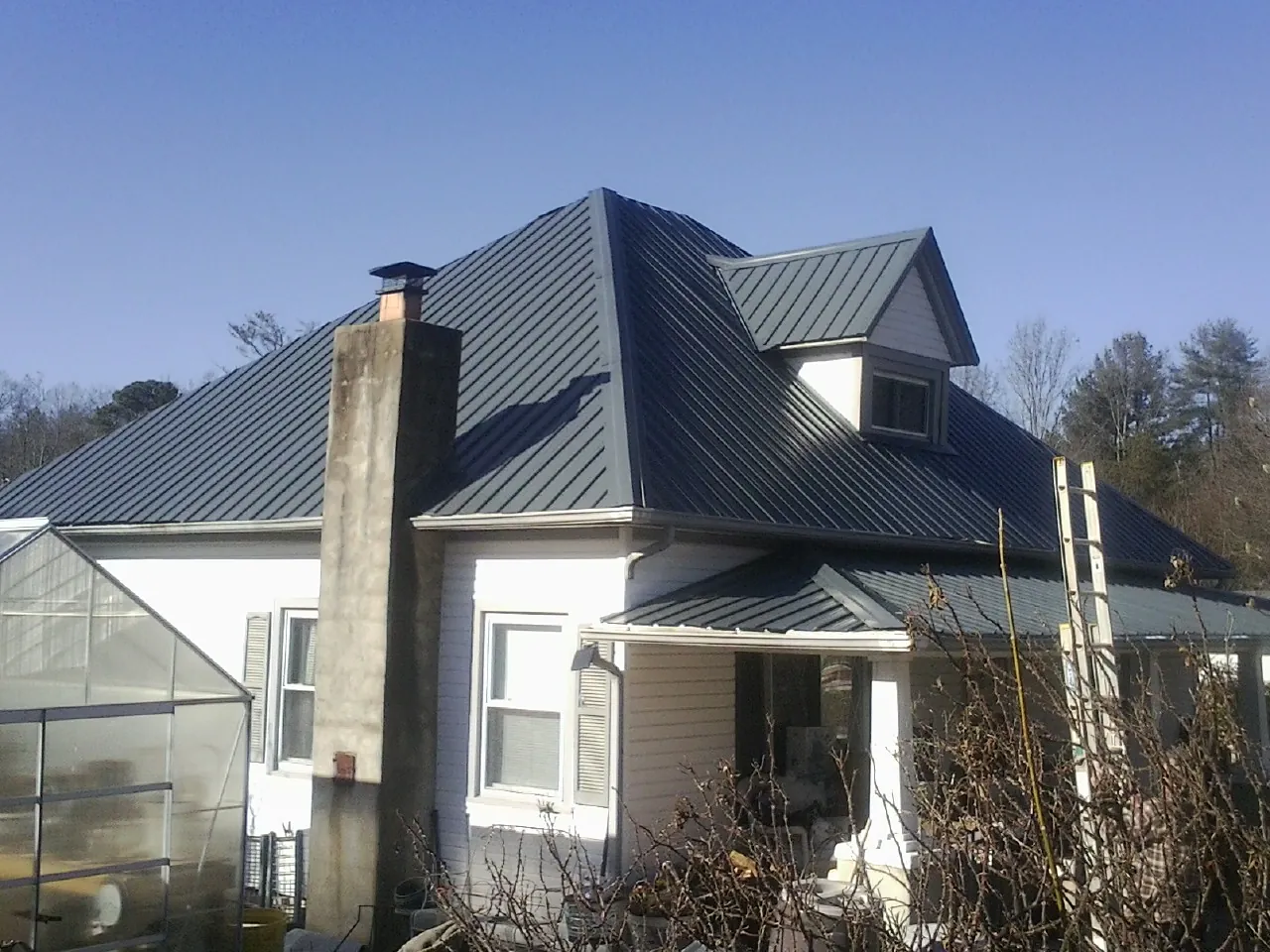 Dark blue standing seam metal roof on a white farmhouse with dormer — Slate & Tile Roof Repair by Roofing Brothers in Port Murray