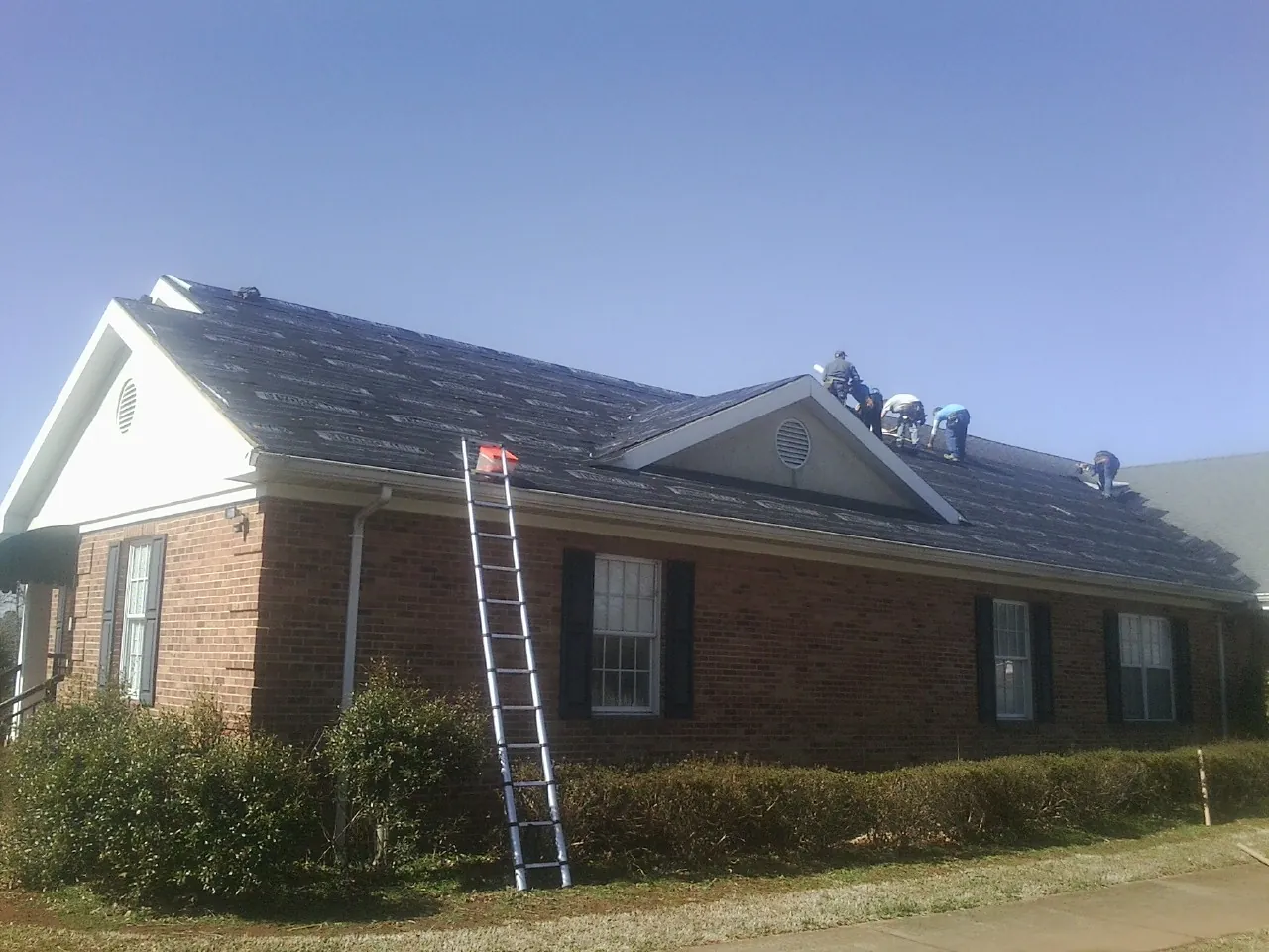 Crew tearing shingles off a brick ranch roof with a ladder set — Emergency Roof Repair work by our crew in Port Murray