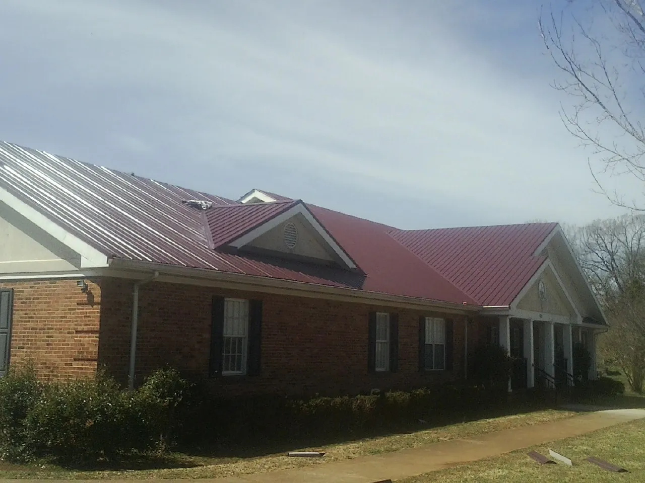 Red metal roof with gabled entries on a long brick building, from a Hail Damage Roof Repair job in Port Murray