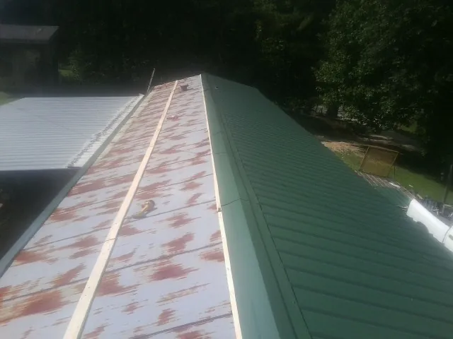 Old rusted panels beside newly installed green metal roofing — Wind Damage Roof Repair by Roofing Brothers in Port Murray
