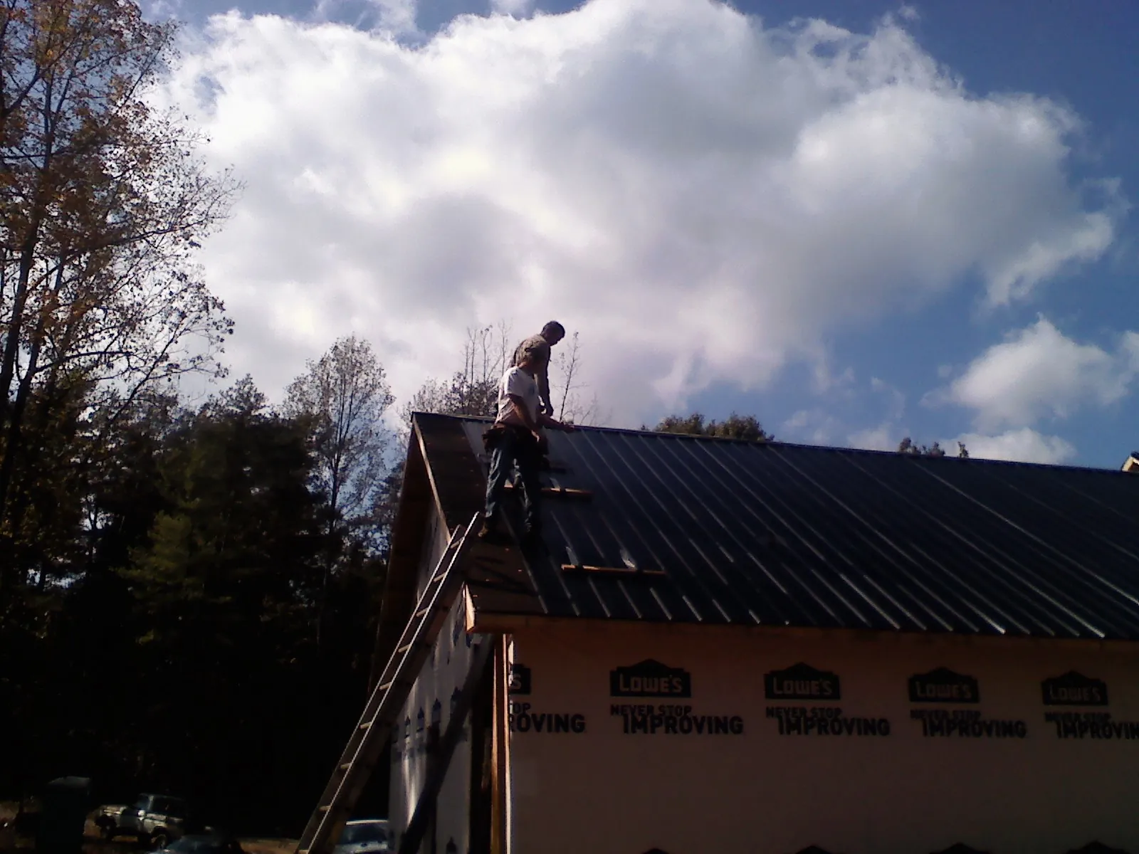 Roofer fastening dark metal panels high against a cloudy sky, from a Roof Inspection job in Port Murray