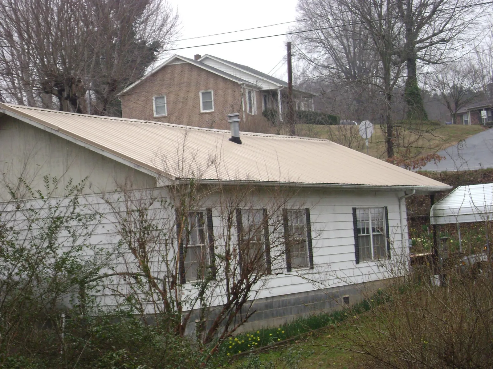 Tan metal roof on a white sided house set into a hillside — Commercial Roofing by Roofing Brothers in Port Murray